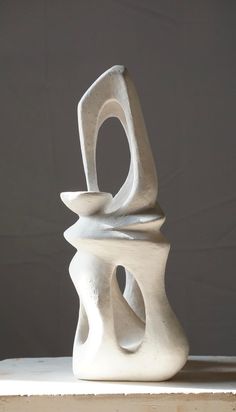 a white sculpture sitting on top of a wooden table next to a gray wall in the background