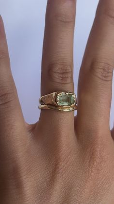 a woman's hand with a gold ring and an oval shaped green stone on it