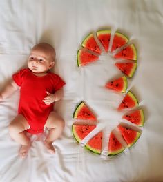 a baby is laying on a bed with slices of watermelon in the shape of a circle