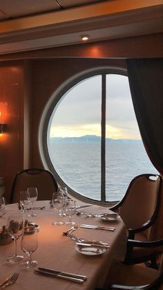 a table set with wine glasses and silverware in front of a large window overlooking the ocean