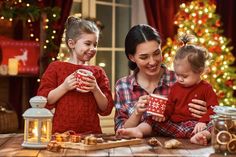 two women and a child are sitting at the table in front of christmas tree with gifts