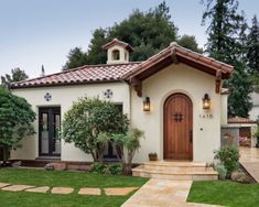 a white house with a brown door and steps leading up to the front entrance is surrounded by greenery