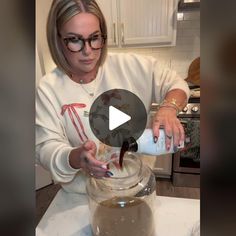 a woman is pouring something into a glass bowl with liquid in it on a counter