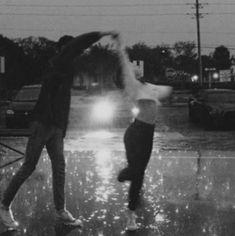 two people jumping in the air on a wet street at night with their arms outstretched