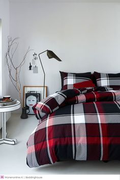 a bed with red and black plaid comforter in a bedroom next to a window