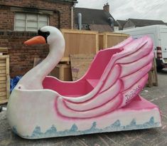 a pink and white swan shaped float sitting on the side of a road in front of a brick building