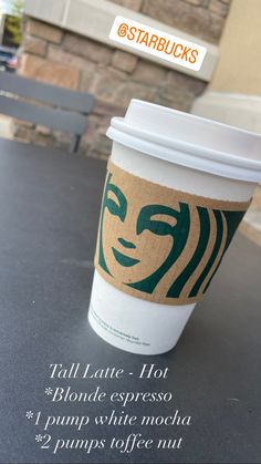 a coffee cup sitting on top of a table next to a brick building with the words starbucks written below it