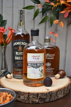 two bottles of whiskey sitting on top of a wooden table next to some nuts and flowers