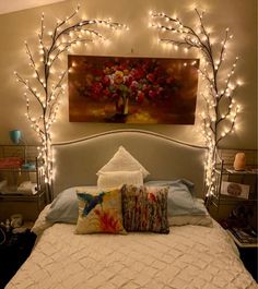 a white bed topped with lots of pillows and lights next to a painting on the wall