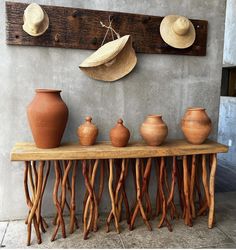 a wooden table topped with vases next to a wall mounted hat rack filled with hats