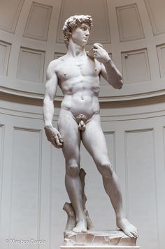 a statue of a man with no shirt on standing in front of a white wall