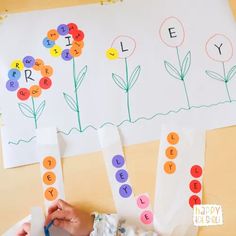 a child's hand is writing letters on paper with flowers in the background and another person holding a pair of scissors