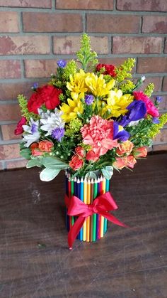 a vase filled with colorful flowers on top of a wooden table next to a brick wall