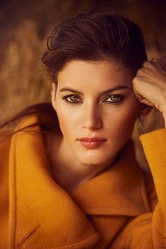 a woman in a yellow coat posing for the camera with her hand on her head