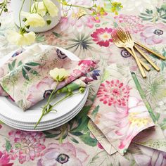 a table topped with plates and napkins covered in floral print cloth next to flowers