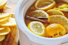 lemons and cinnamon sticks are in a white crock pot filled with liquid on a wooden table