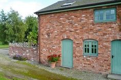 an old brick building with green doors and flowers in the window boxes next to it