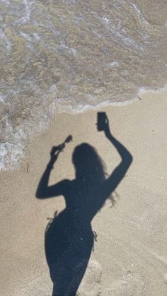 the shadow of a woman on the beach holding a cell phone up to her head