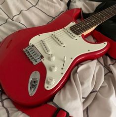 a red electric guitar laying on top of a bed