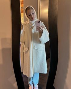 a woman taking a selfie in front of a mirror wearing slippers and a coat