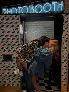 two people kissing each other in front of a photo booth with black and white checkered walls