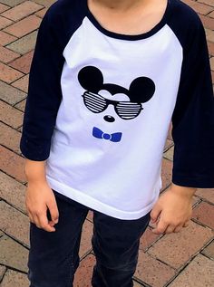 a young boy wearing sunglasses and a mickey mouse t - shirt stands in front of a brick walkway