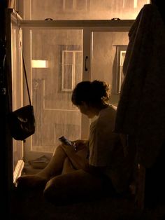 a woman sitting on the floor looking at her cell phone in front of a window