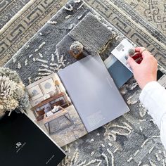 a person is holding an open book on the floor next to rugs and pillows