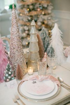 the table is set with pink and silver christmas trees, candles, and place settings