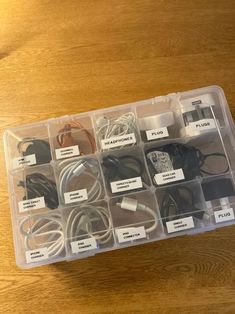 an open plastic box filled with various electrical cords and plugs on top of a wooden table