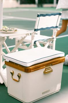 Elegant white cooler with wood and brass accents serving as versatile outdoor seating by the tennis court, paired with stylish tableware.