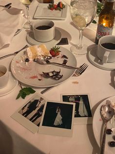 a table topped with plates and cups filled with food next to wine glasses on top of a white table cloth