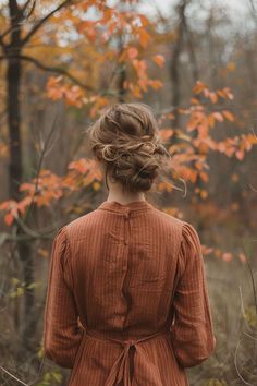 a woman standing in the woods with her back to the camera, wearing an orange dress