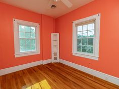 an empty room with orange walls and wood floors, two windows on the far wall