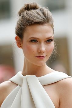 a woman wearing a white dress with a high bun in her hair and looking at the camera