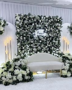 a white couch sitting in front of a wall covered in flowers and greenery next to candles