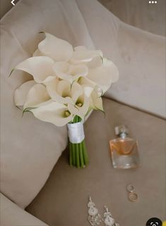 a bouquet of white flowers sitting on top of a couch next to a perfume bottle