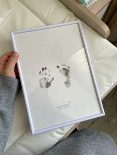 a person holding up a framed photo with two baby footprints