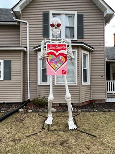 a skeleton holding a heart shaped card in front of a house with the word love on it