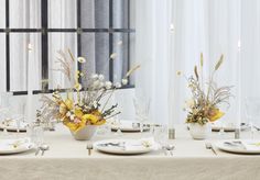 the table is set with white plates and silverware, yellow flowers in vases