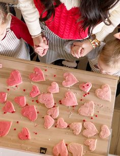 two children and an adult are making heart shaped cookies on a wooden board with pink icing