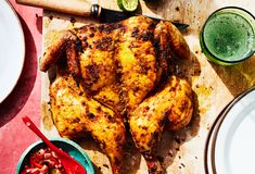 a whole chicken sitting on top of a wooden cutting board next to plates and knives