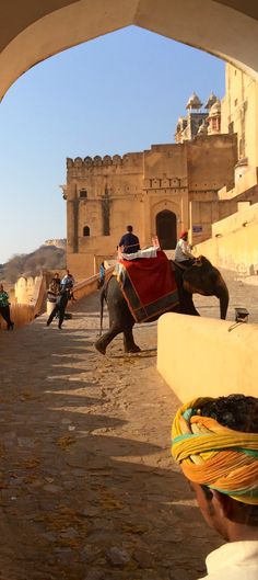 people riding on the backs of elephants in front of an old city wall and gate