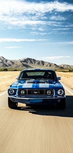 a blue muscle car driving down the road with mountains in the background