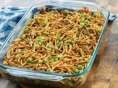 a glass casserole dish filled with noodles and peas sitting on a wooden table