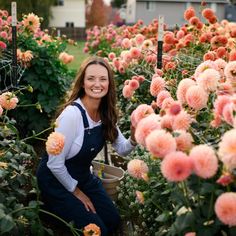 a woman in an apron is kneeling down among many pink flowers and holding a bucket