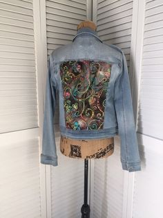 a denim jacket with an intricate design on the front and back, sitting on top of a mannequin