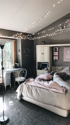 a bedroom with lights strung above the bed and desk in front of it, next to a window