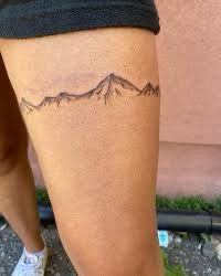 a woman's leg with a tattoo on it that has mountains in the background