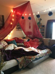 an unmade bed with red curtains and lights on the headboard, in a bedroom